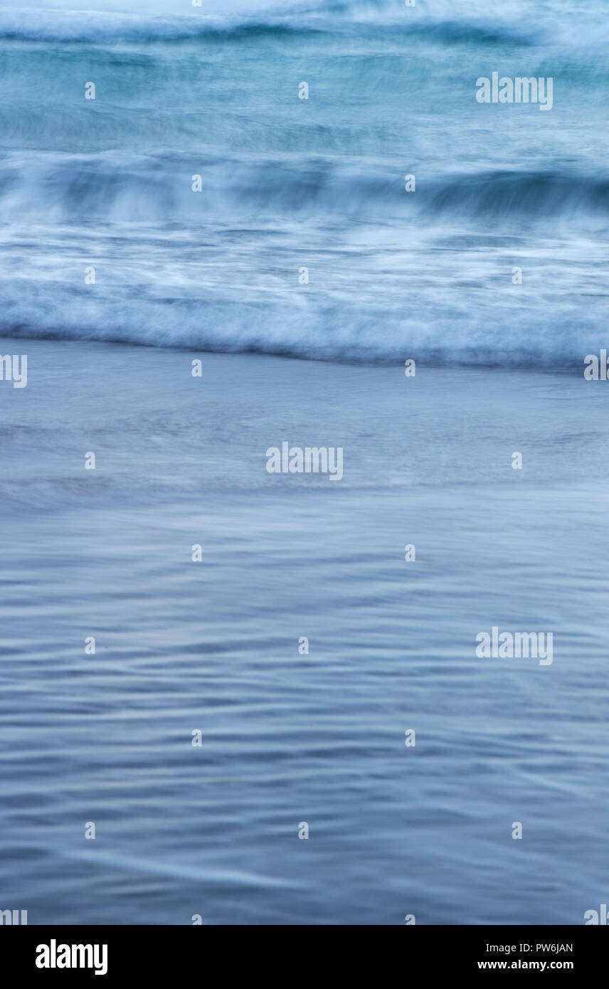 Una lunga esposizione delle onde e la marea schizzi su una spiaggia di sabbia Foto Stock