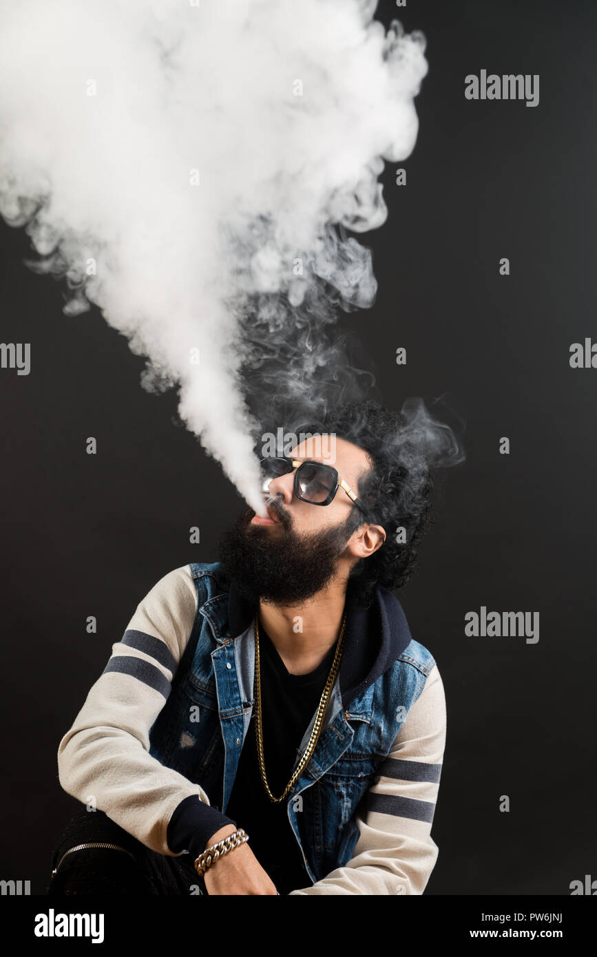 Giovane uomo con la barba vaping una sigaretta elettronica verso l'alto. Tanga Vaper vaporizzatore di fumo. Sfondo nero Foto Stock