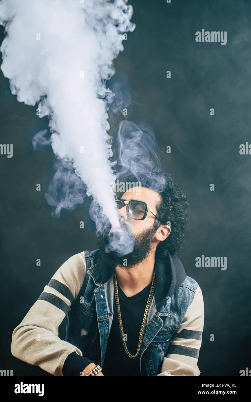 Giovane uomo con la barba vaping una sigaretta elettronica verso l'alto. Tanga Vaper vaporizzatore di fumo. Sfondo nero Foto Stock