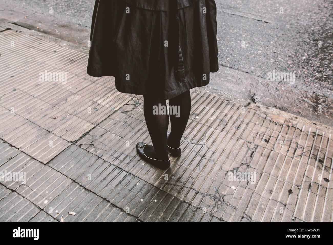 Donna vestita di nero in attesa da solo in condizioni di bagnato marciapiede Foto Stock