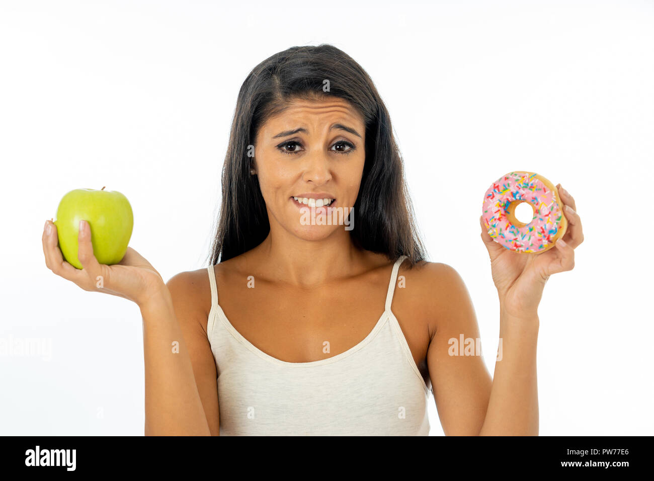 Bella giovane donna tentati di dover fare una scelta tra apple e la ciambella in sano cibo malsano, detox mangiare, calorie e il concetto di dieta. Foto Stock