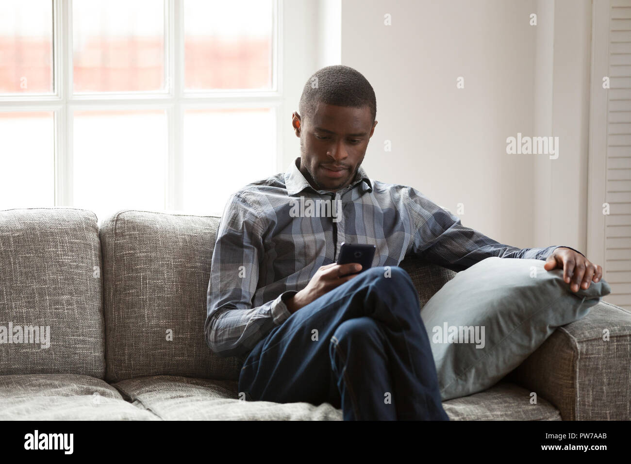 Uomo nero con telefono seduti sul divano di casa Foto Stock