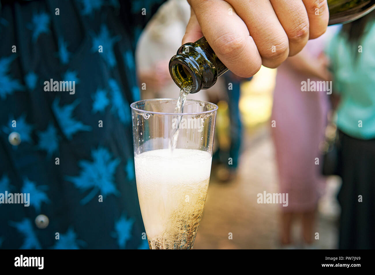 Una chiusura di un half-filled calice di champagne detenute da un uomo al outdoor evento festivo. Il maschio degli ospiti di nozze riempie il bicchiere di vino spumante Foto Stock