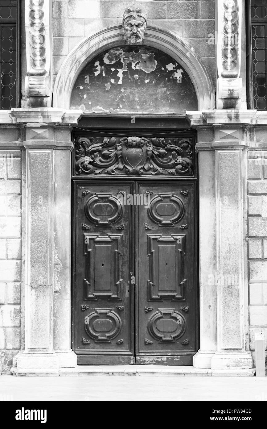 Porta nera nella parte esterna di un vecchio edificio bianco con pietre di marmo e due statue poste sui lati, la fotografia in bianco e nero Foto Stock
