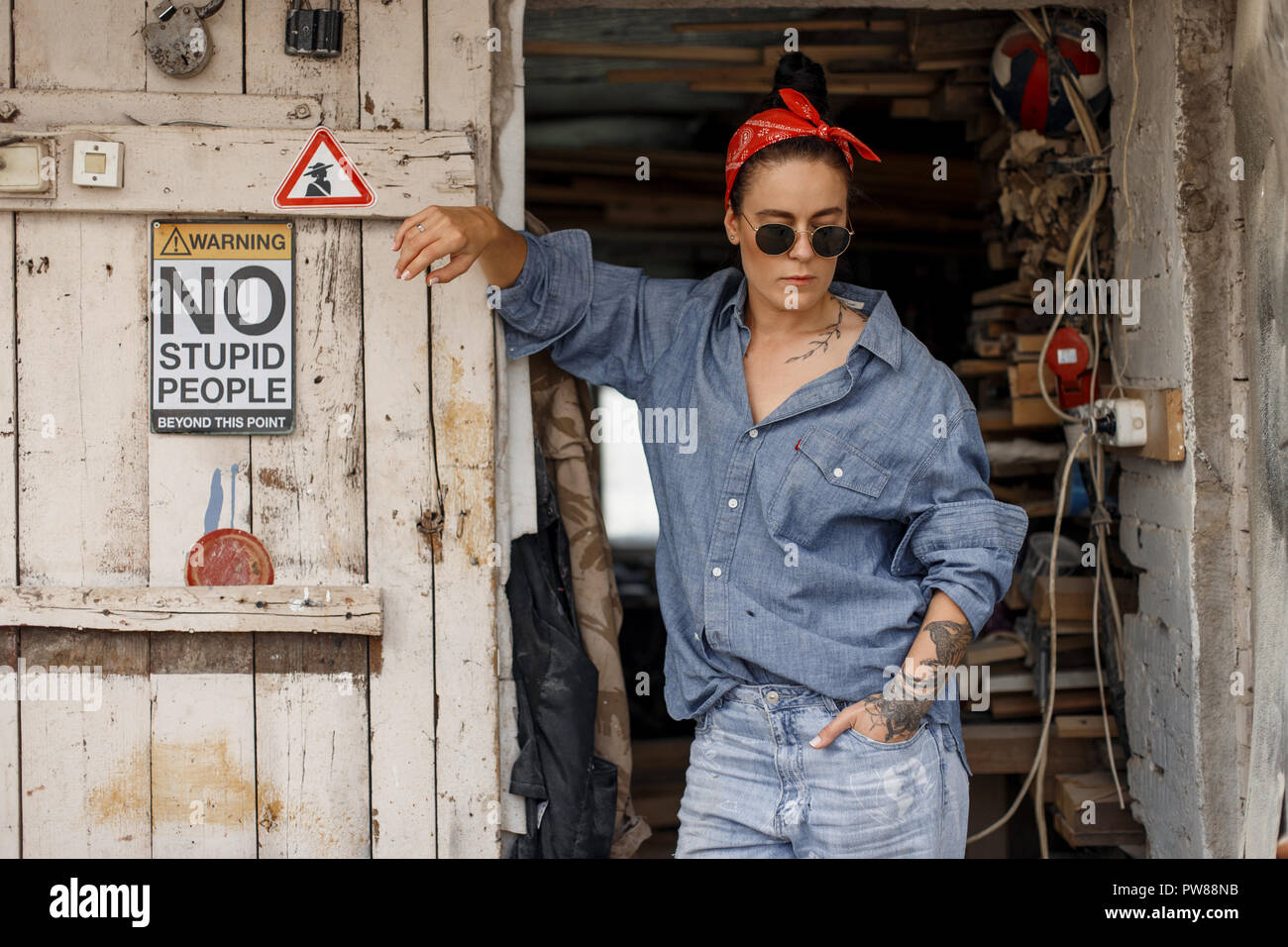 Elegante bella donna americana con occhiali da sole di tessuto in jeans  abiti alla moda e jeans sorge in prossimità di un legno porta vintage Foto  stock - Alamy