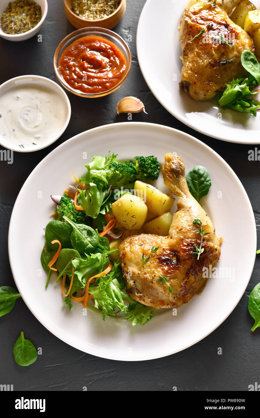 Pollo alla griglia della gamba con patate e insalata verde sulla pietra nera dello sfondo. Piatto per la cena. Vista superiore Foto Stock
