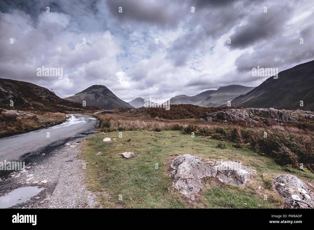 Strada di campagna con poche pozzanghere dopo la pioggia trogolo scenic valle di montagna con vista sulle cime del Cumbria rurale nel Nord Ovest Inghilterra.drammatico cielo sopra mou Foto Stock