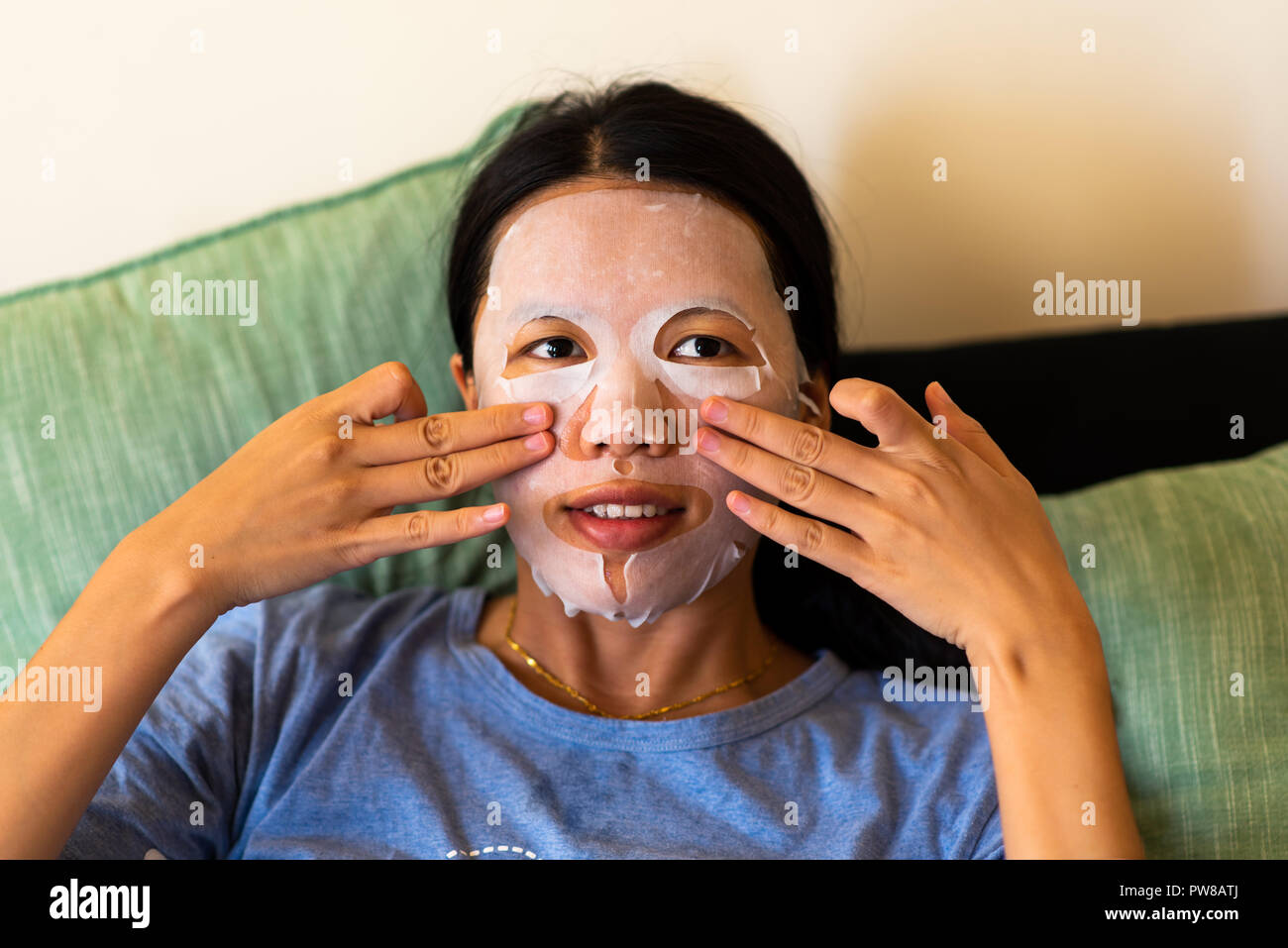 Donna asiatica di applicare la maschera per il viso a casa Foto Stock