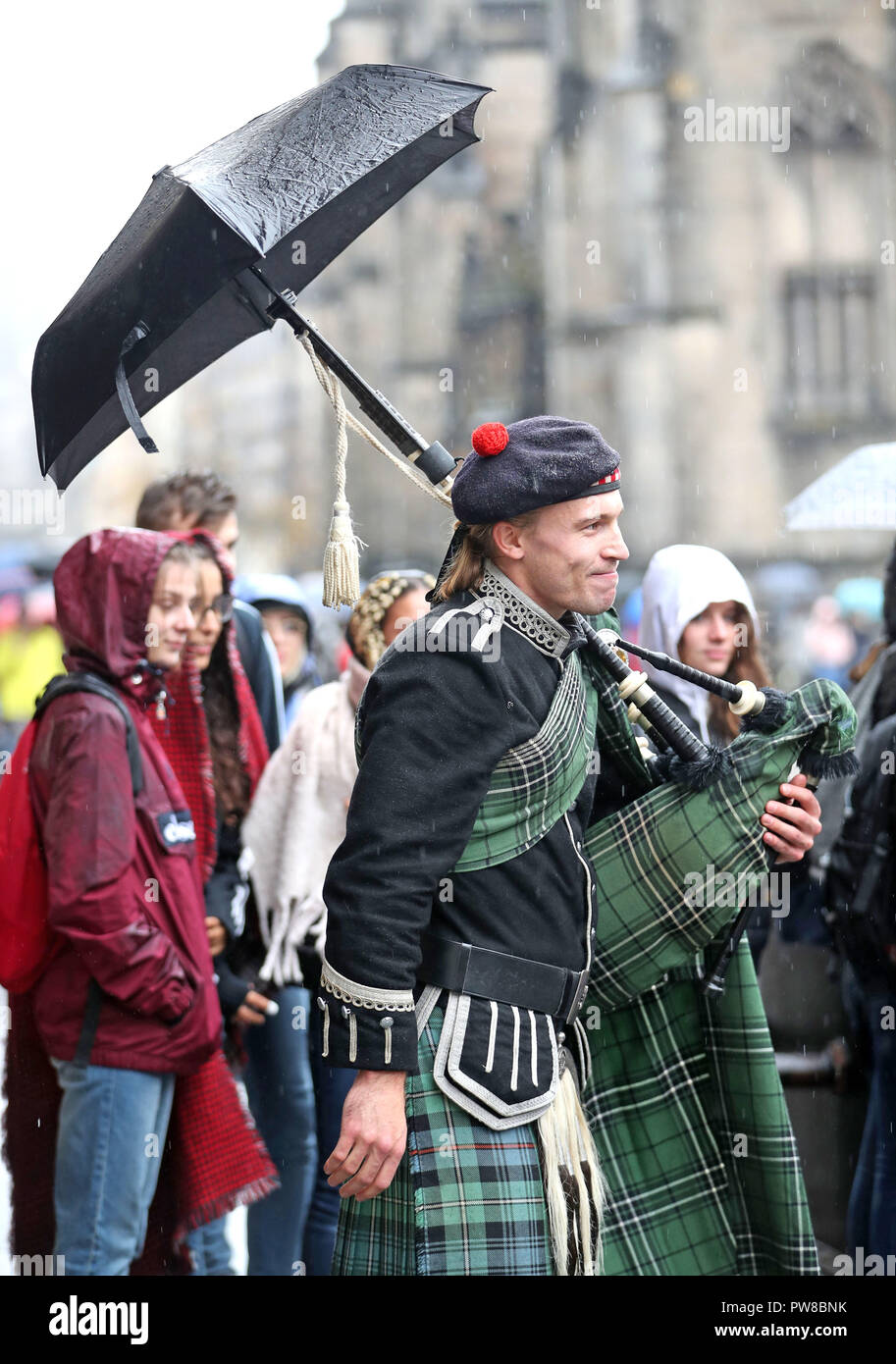 Un piper, con un ombrello attaccato alla sommità del suo tubazioni, intrattiene la folla sotto la pioggia su Edinburgh Royal Mile. Foto Stock