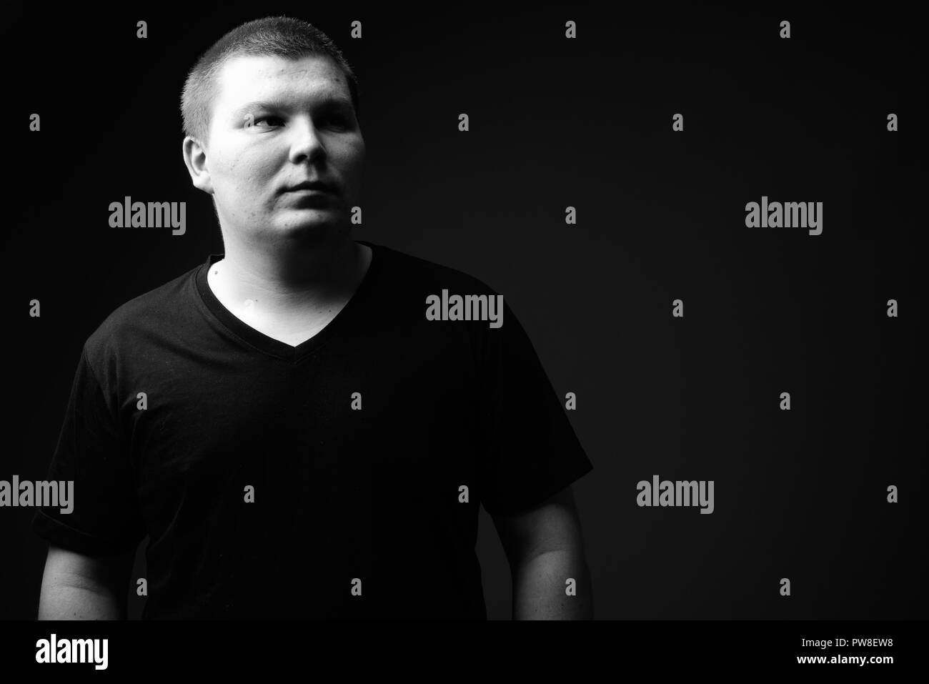 Il sovrappeso giovane uomo contro lo sfondo nero in bianco e nero Foto Stock