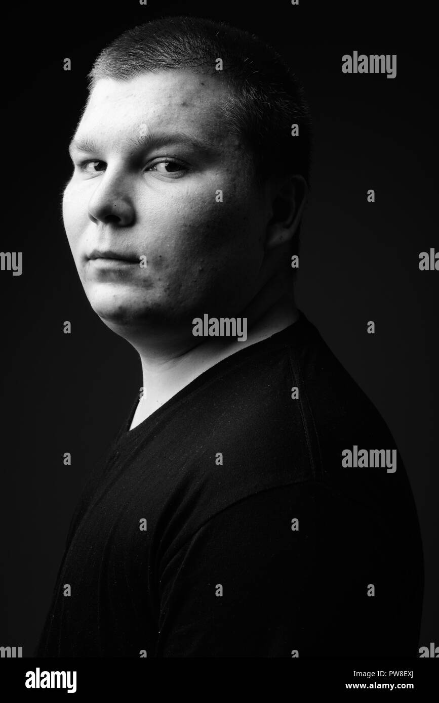 Il sovrappeso giovane uomo contro lo sfondo nero in bianco e nero Foto Stock