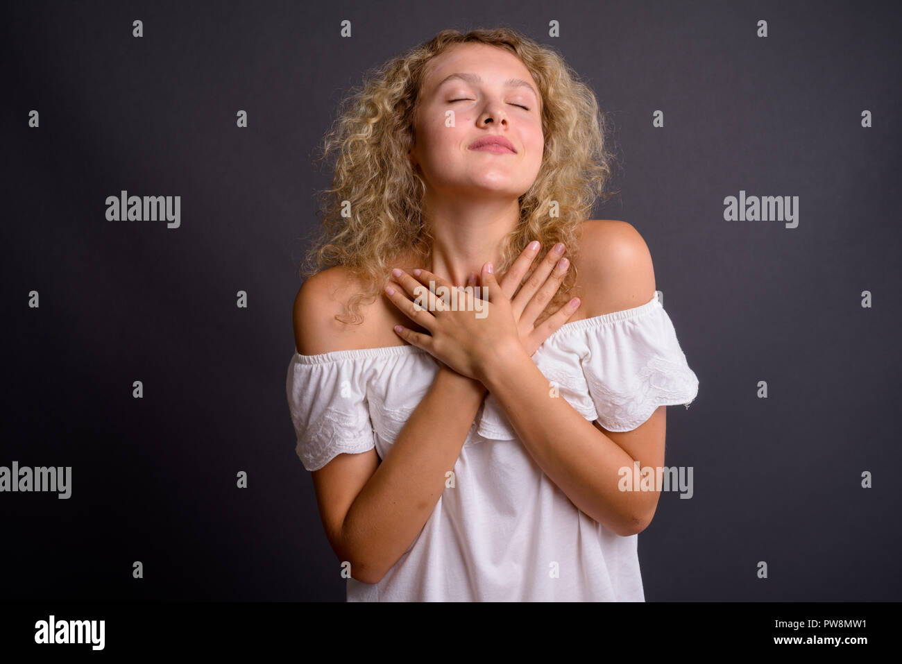 Giovane bella donna bionda con capelli ricci contro backgro grigio Foto Stock