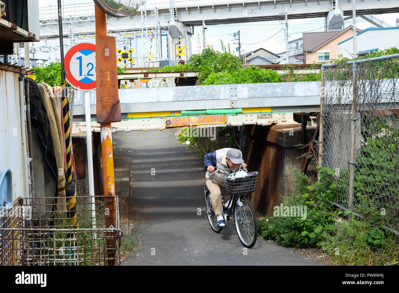 Molto basso di ponte di Osaka in Giappone. Un binario ferroviario passa il sovraccarico di lavoro con persone aventi per duck per evitare il 120-cm-alta barra metallica di cui sopra. Foto Stock