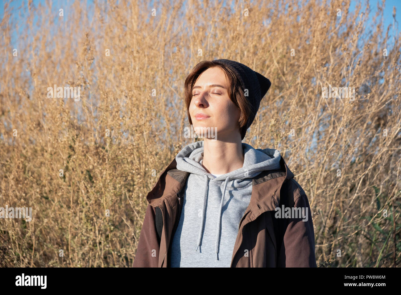 Giovane donna gode del sole autunnale. Femmina in parka all'aperto sul luminoso pomeriggio soleggiato Foto Stock