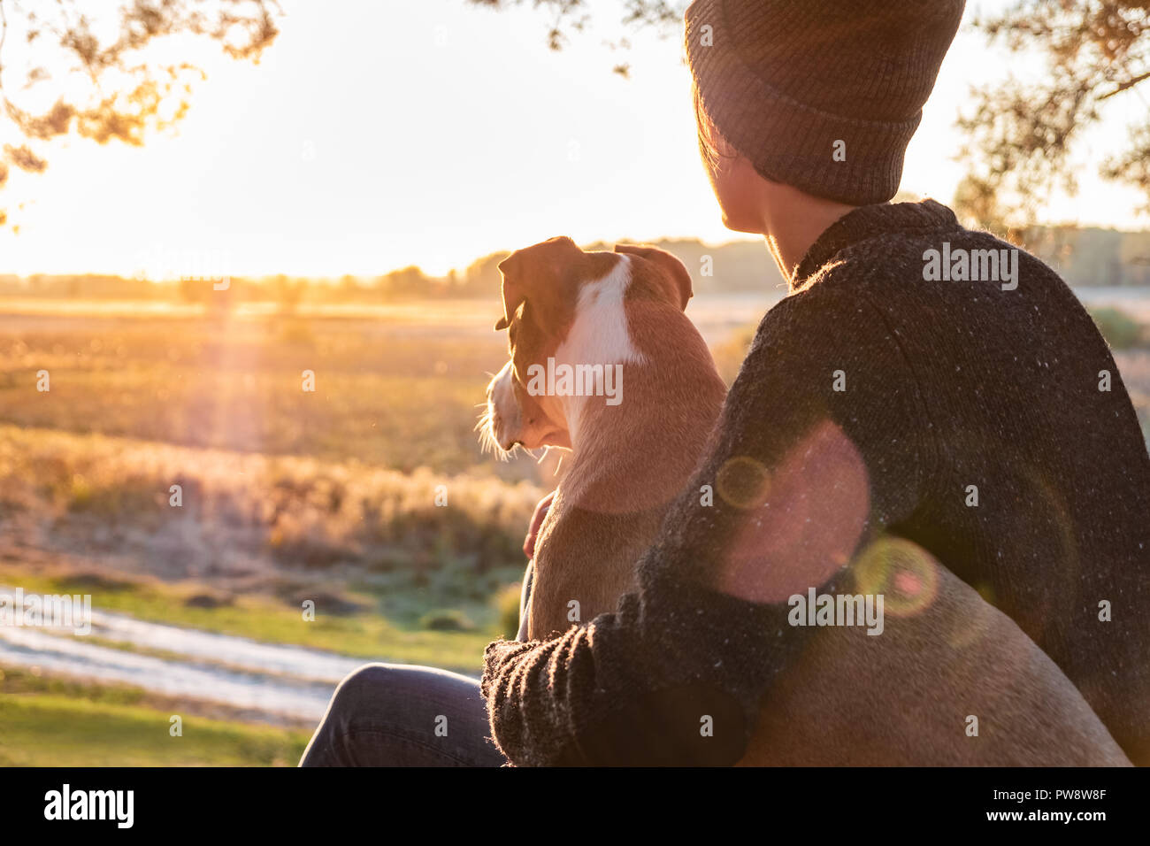Abbracciando un cane nella bellissima natura al tramonto. La donna rivolta verso il sole di sera si siede con il suo animale domestico accanto a lei e che gode la bellezza di Natura Foto Stock