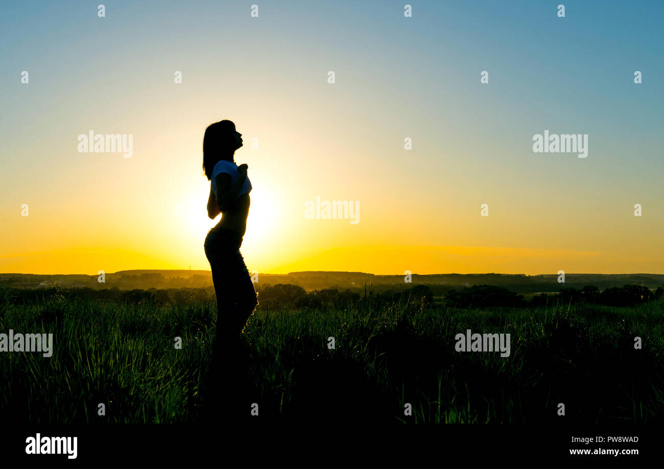 Silhouette di una giovane donna davanti a un bel tramonto. Donna sensuale con il sole che si alza dietro di lei. Foto Stock