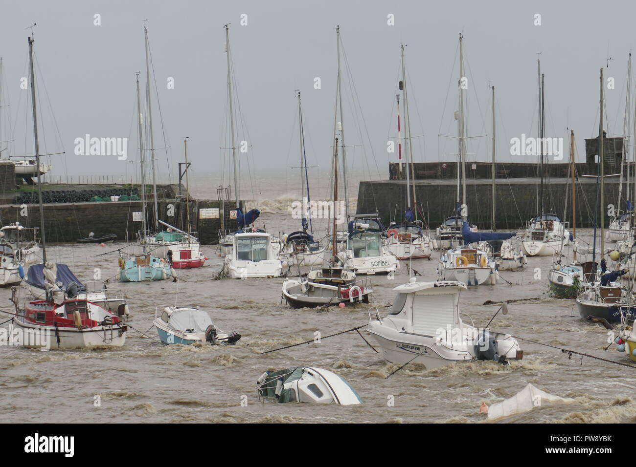 Aberaeron, UK. 13 ottobre 2018. Una scena di devastazione in Aberaeron Harbour sulla West Wales coast questo pomeriggio come heavy rain e alta venti di tempesta Callum continuare a causa della distruzione. Acqua di inondazione dal fiume Aeron alberi portanti e grossi rami in crash barche ormeggiate ci danno a molti e totalmente naufragio altri. Credito: Anthony Pugh/Alamy Live News Foto Stock