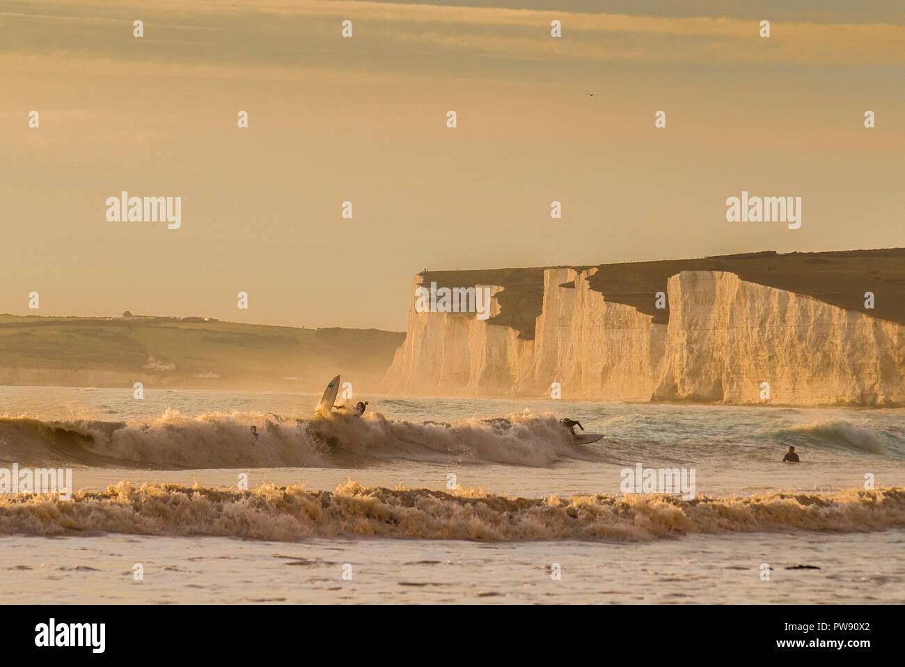 Birling Gap, Eastbourne, East Sussex, Regno Unito..13 ottobre 2018.. Una splendida serata balmy con vento caldo dal sud. Surfers contro la magnifica goccia posteriore delle scogliere di gesso di Seven Sisters. ... Foto Stock