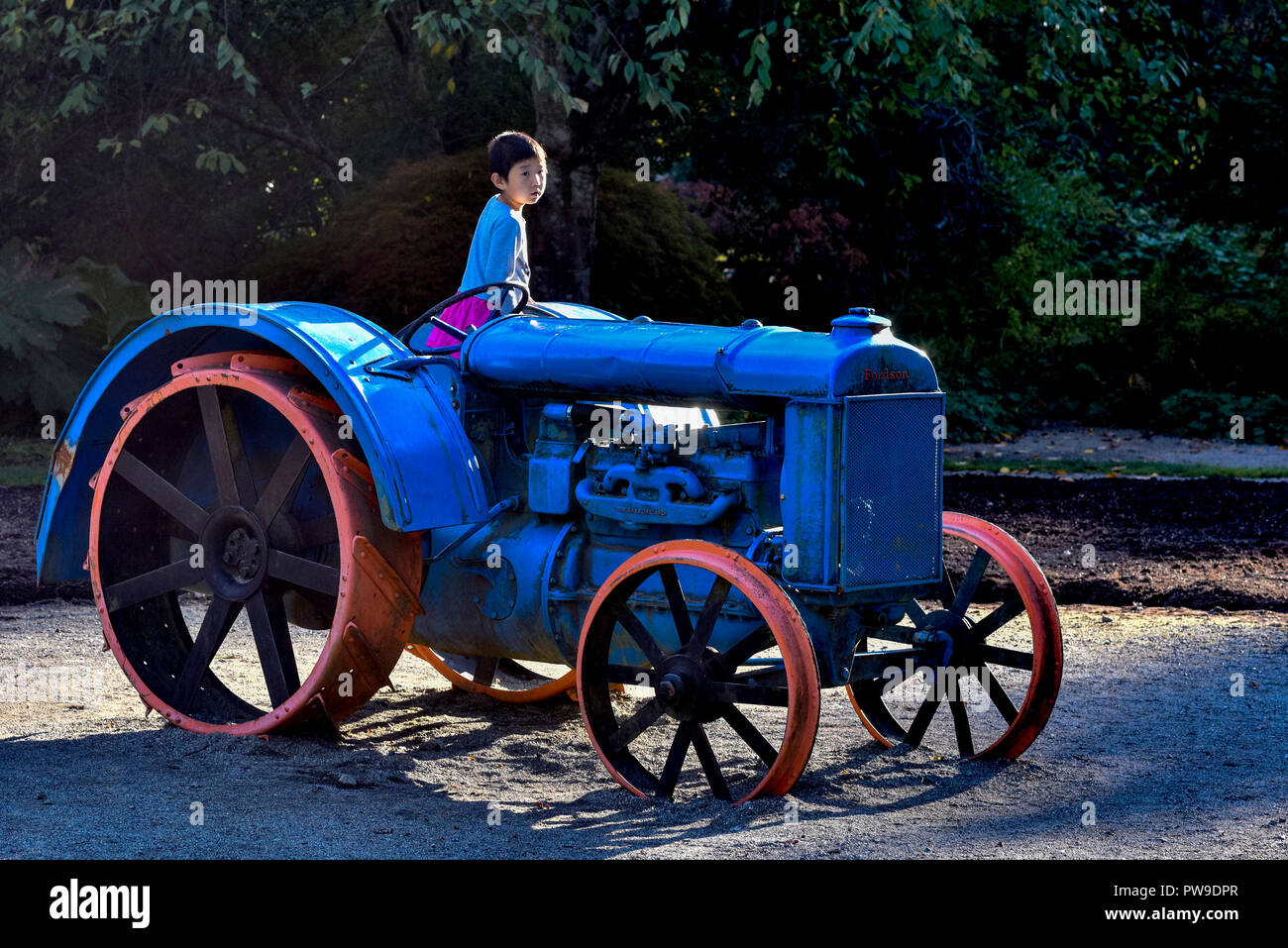 Ragazzo asiatico sul vecchio trattore agricolo, Van Dusen giardino, Vancouver, British Columbia, Canada Foto Stock