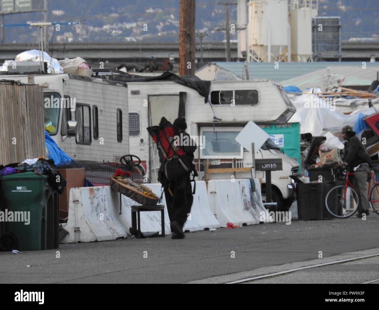 Un uomo cammina da un grande senzatetto encampment su Wood Street nella zona ovest di Oakland. Foto Stock