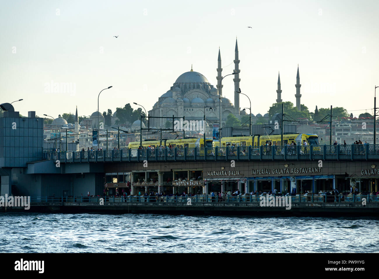 Un giallo il tram passa sopra il ponte Galata con la moschea di Suleymaniye in background, Istanbul, Turchia Foto Stock