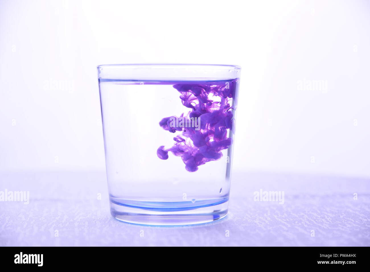 Vetro con acqua su uno sfondo bianco con vernice viola Foto Stock