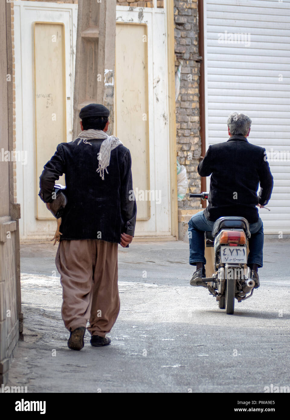 Yazd, Iran - Marzo 7, 2017 : scena quotidiana in uno stretto vicolo della Città Vecchia. Uomo in sella a una motocicletta. Uomo con un pollo Foto Stock