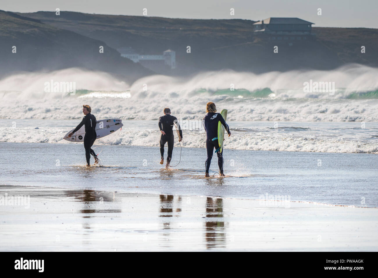 Surfers che trasportano le loro tavole da surf a piedi in mare a Fistral Beach in Newquay in Cornovaglia. Foto Stock