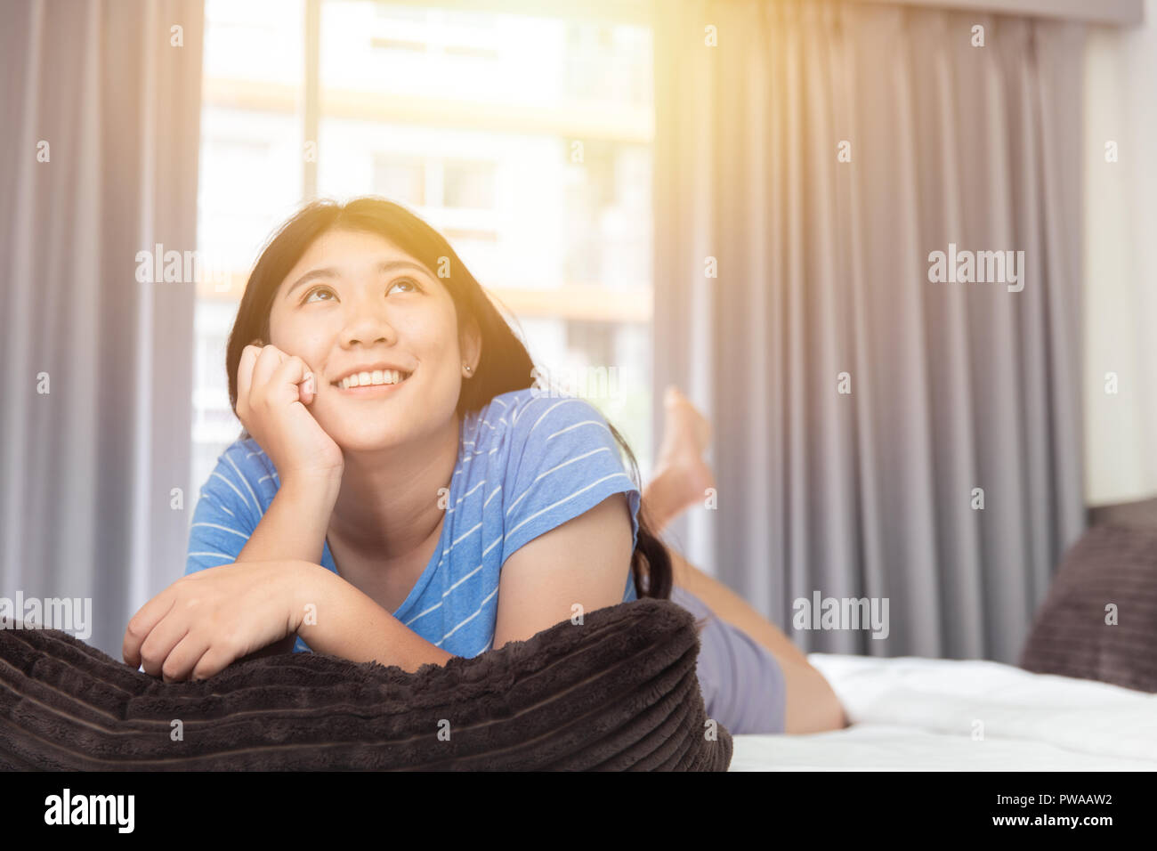 Carino ragazza asiatica teen giorno pigro mano a mento sul letto cercando di alta pensando mancante fantasticando e sorriso Foto Stock