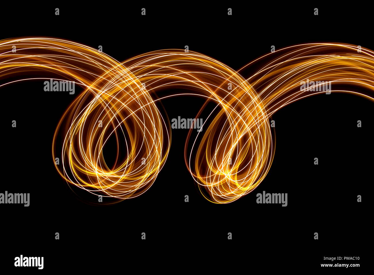 Una lunga esposizione di luce fotografia pittura, curva anse di vibrante metallico al neon giallo oro su sfondo nero Foto Stock