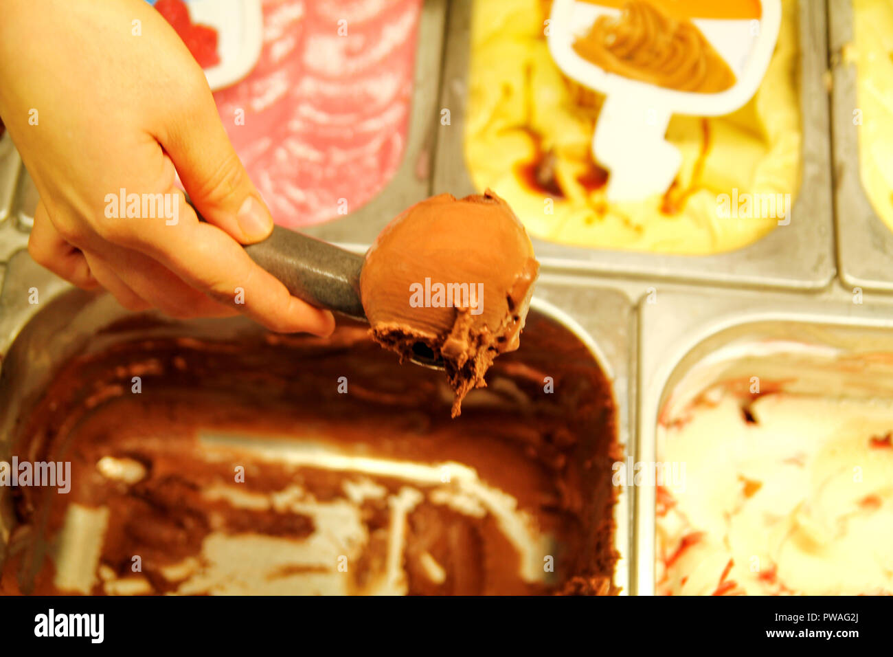 Mano femmina con convogliatore prende il gelato di cioccolato dal frigo e servire nel cono di cialda. Donna prendendo scoop di gustoso gelato. Foto Stock