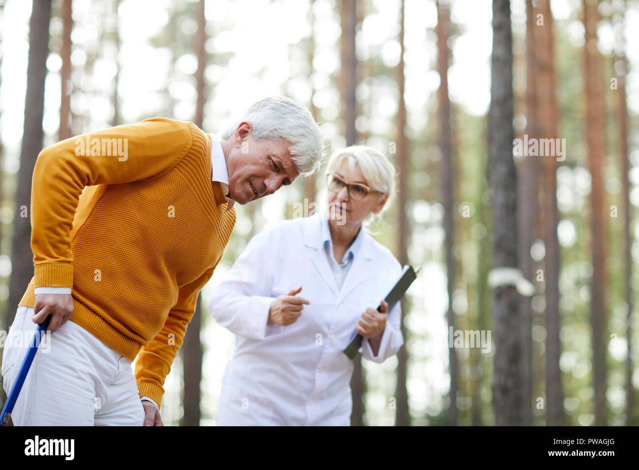 Uomo maturo con il dolore nella gamba muovendo lentamente mentre appoggiata sulla canna, medico in camice bianco consulting lui Foto Stock