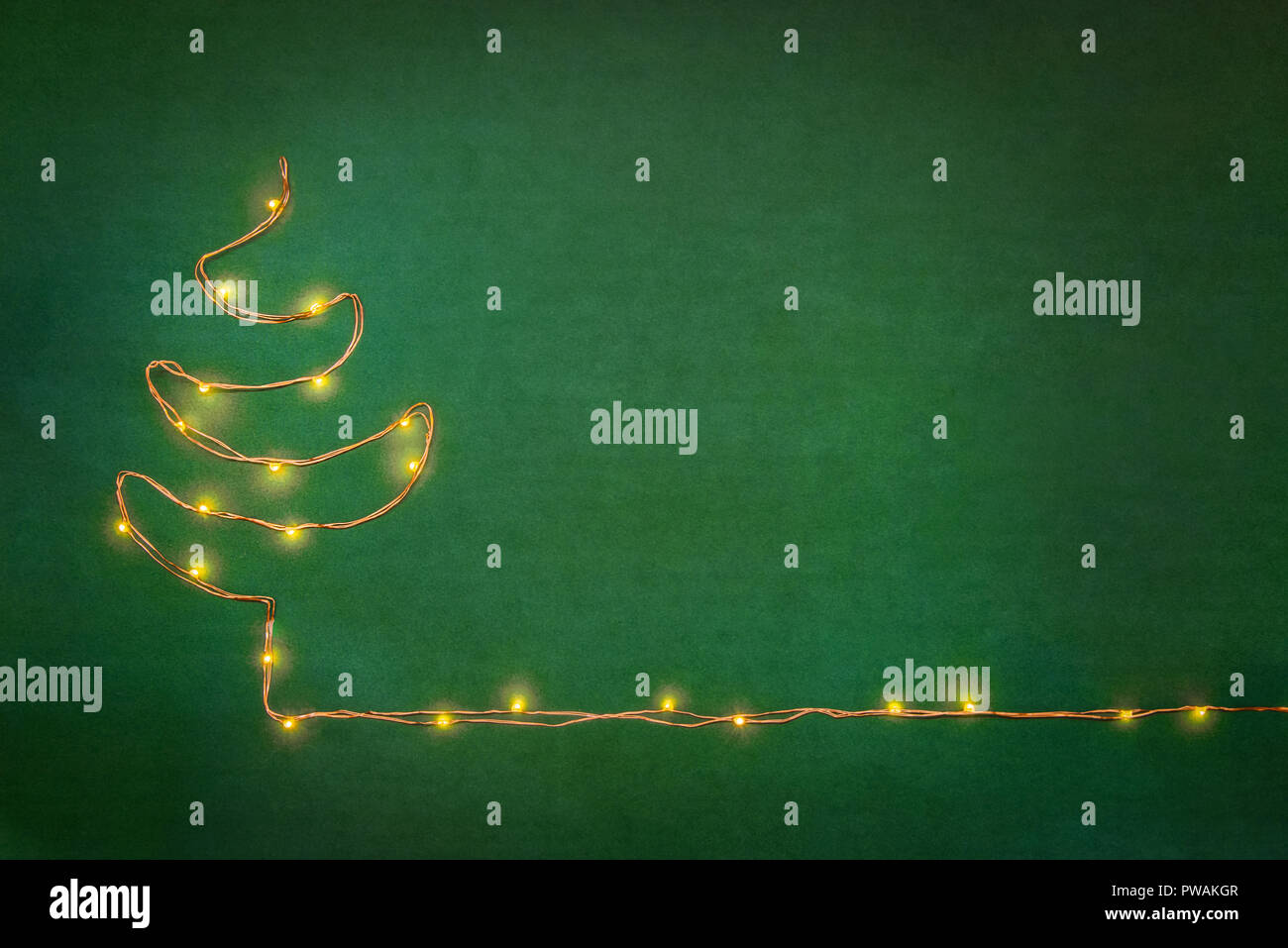 Le luci di Natale ghirlanda disposte come albero di natale su sfondo verde. Laici piana, copia dello spazio. Foto Stock