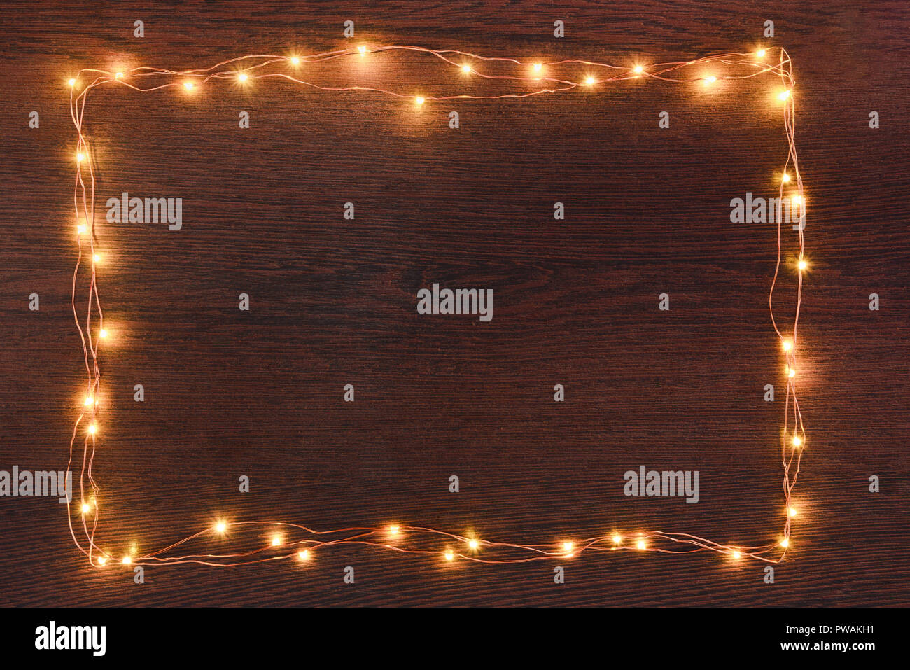 Le luci di Natale ghirlanda oltre confine in legno scuro dello sfondo. Laici piana, copia dello spazio. Foto Stock
