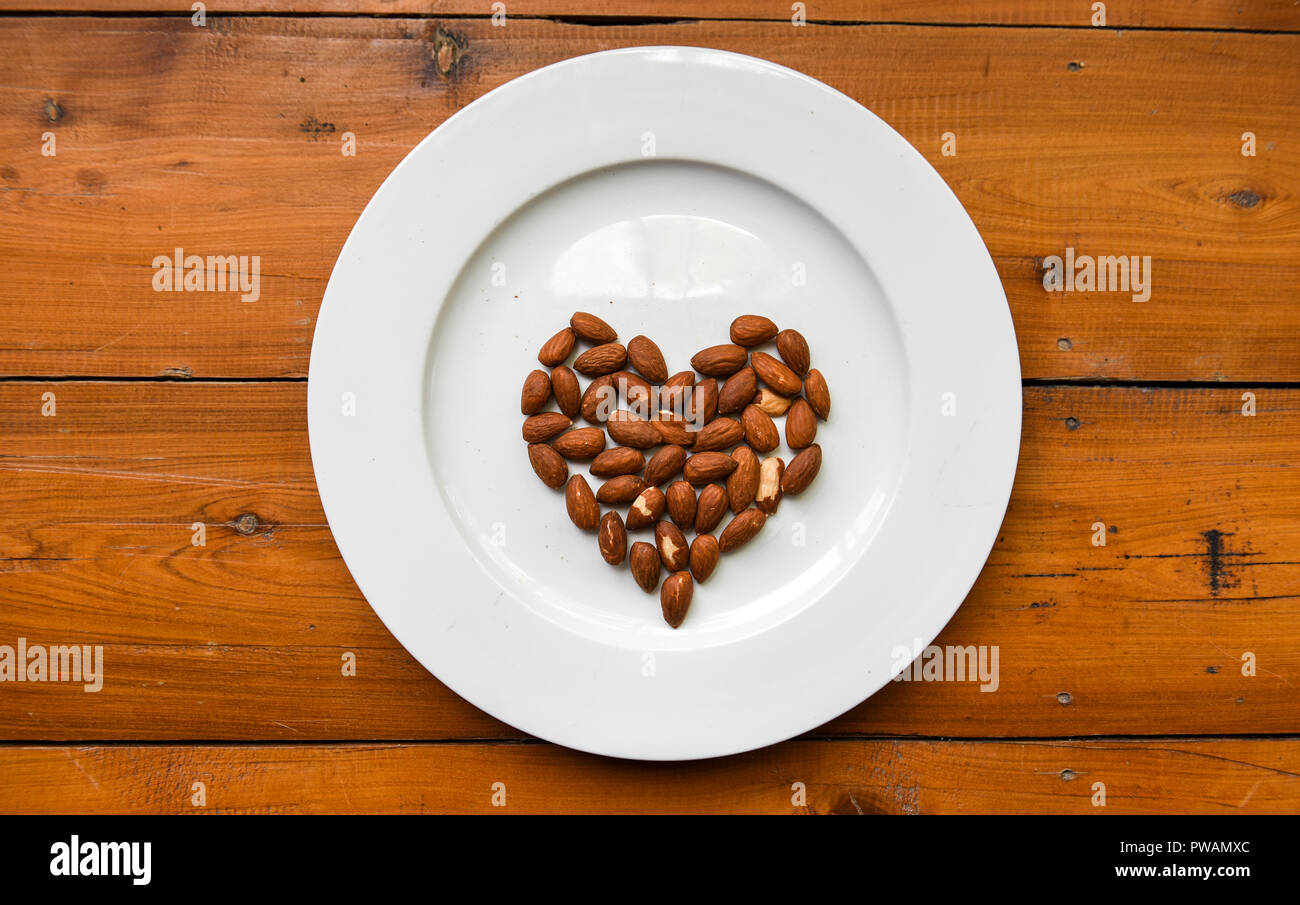 Vista superiore del cuore di mandorle a forma di dadi sul bianco piastra rotonda sul tavolo di legno Foto Stock