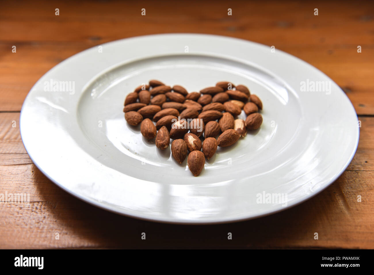Vista laterale del cuore di mandorle a forma di dadi su una bianca piastra rotonda sul tavolo di legno Foto Stock