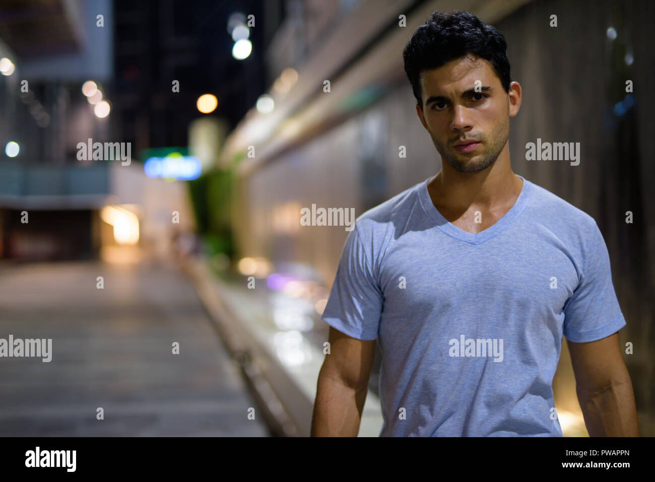 Bel giovane uomo ispanico ad esplorare le strade della città di notte Foto Stock