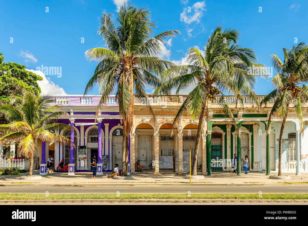 Vecchio stile coloniale spagnolo case colorate con le palme in primo piano, attraversata la strada al centro di Cienfuegos, Cuba Foto Stock