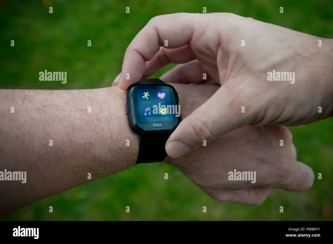 Un uomo controlla il suo Fitbit Versa il tracker di attività compresi monitor frequenza cardiaca utilizzando il BPM di unità durante un esercizio allenamento. Foto Stock
