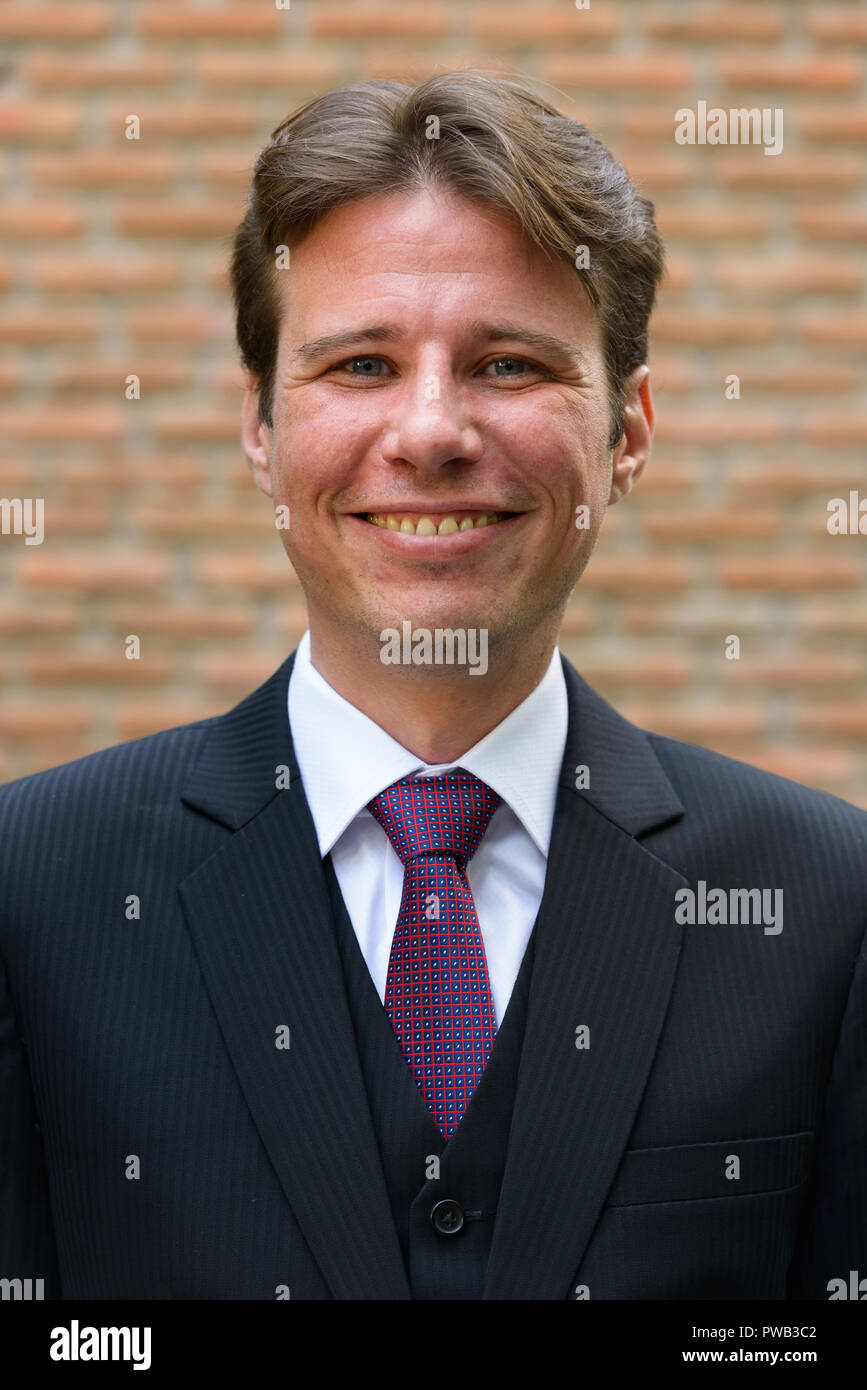 Faccia di happy businessman sorridente contro un muro di mattoni Foto Stock