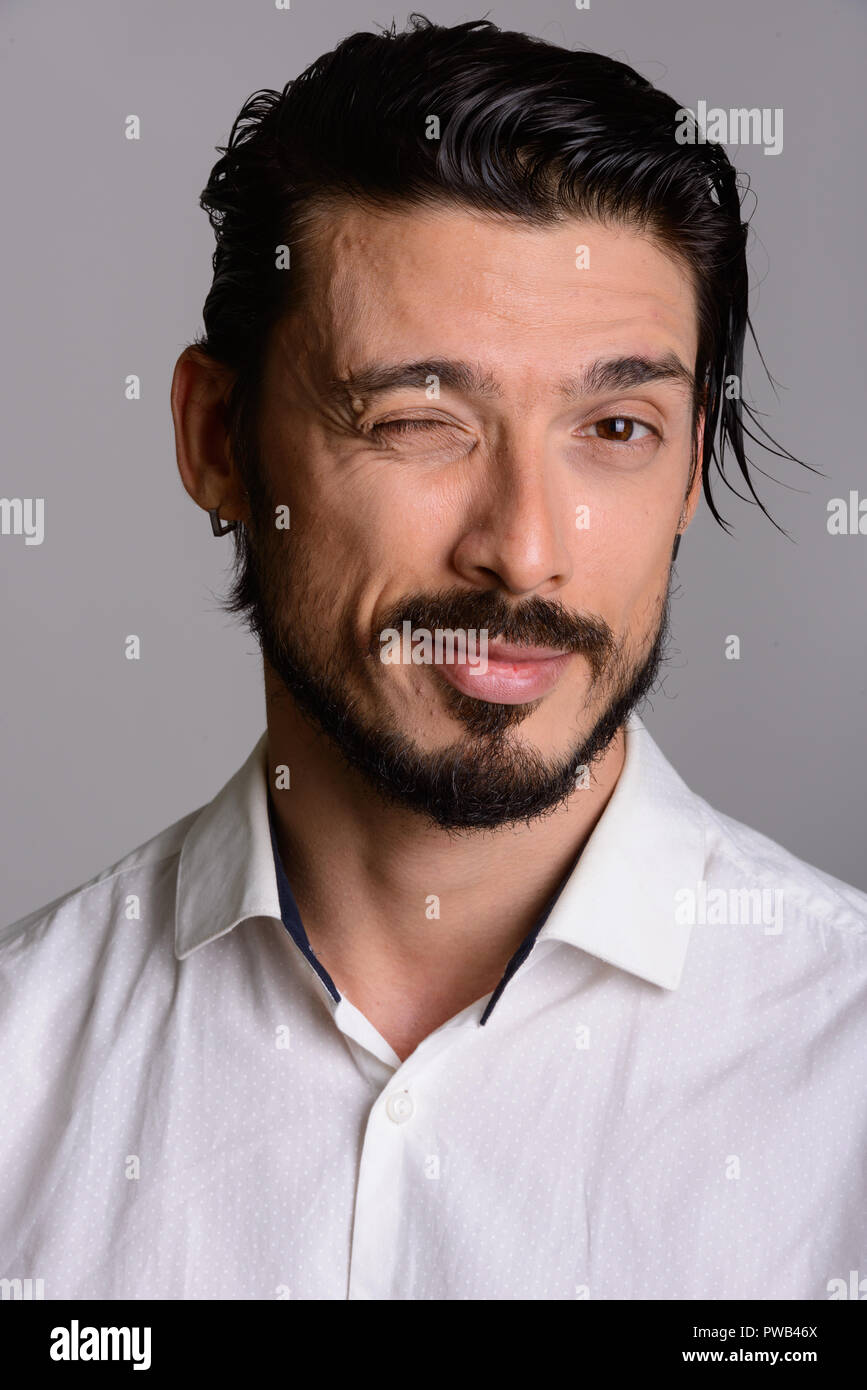Volto di uomo bello winking contro uno sfondo grigio Foto Stock