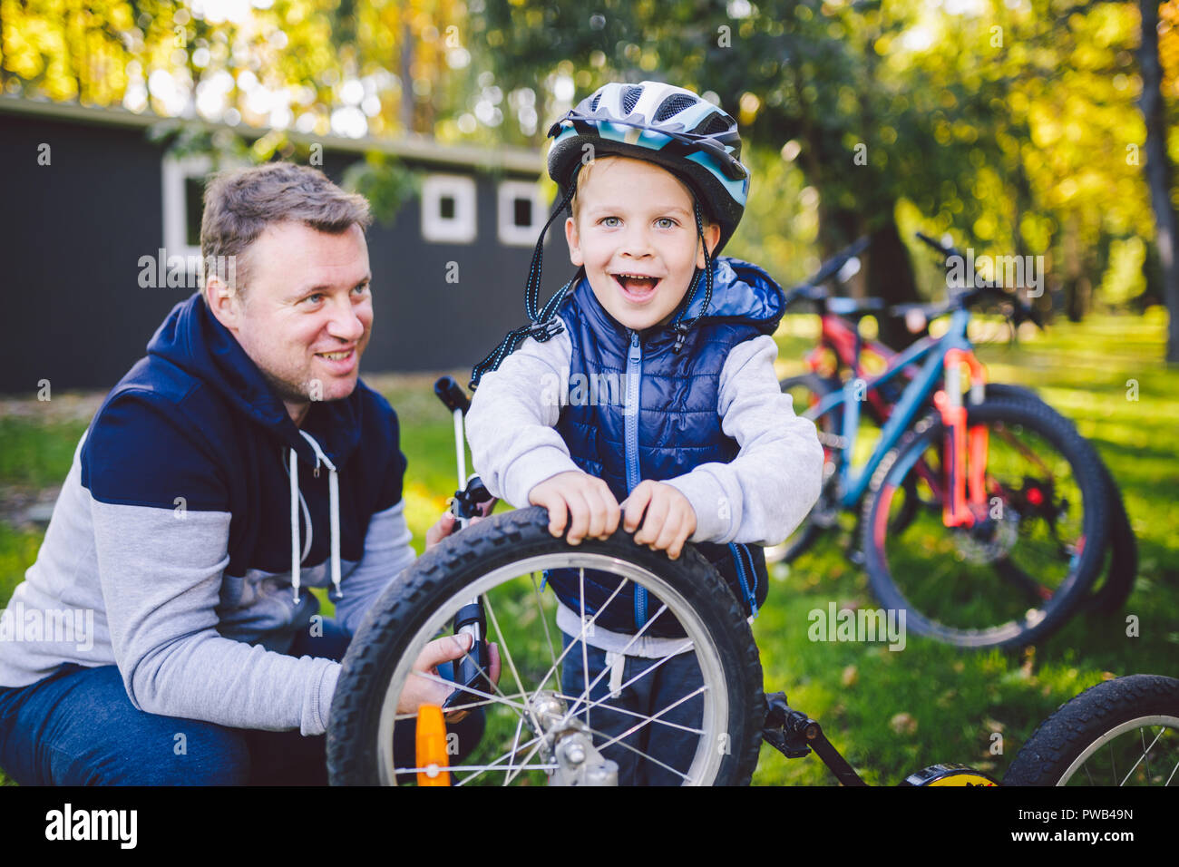 La festa del papà Caucasian papà e figlio di 5 anni nel cortile vicino alla casa sull'erba verde sul prato la riparazione di una bicicletta, di pompaggio di una bicicletta siamo Foto Stock