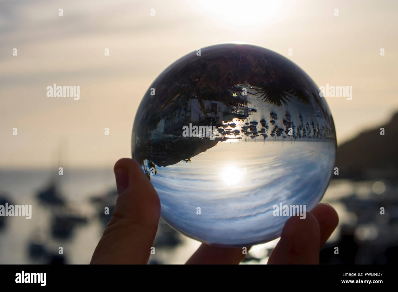 Porto di mare pieno di barche con sole e nuvole catturate in riflessione nella sfera di vetro svoltasi a portata di mano Foto Stock
