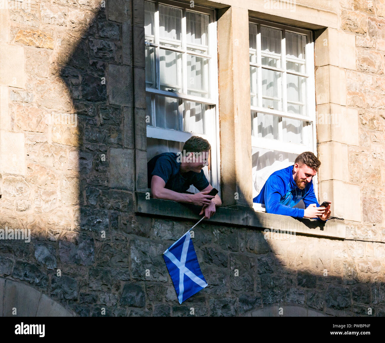 Giovani uomini sporgersi di windows la visione di indipendenza scozzese Tutti sotto uno striscione AUOB marzo, Royal Mile di Edimburgo, Scozia, Regno Unito Foto Stock