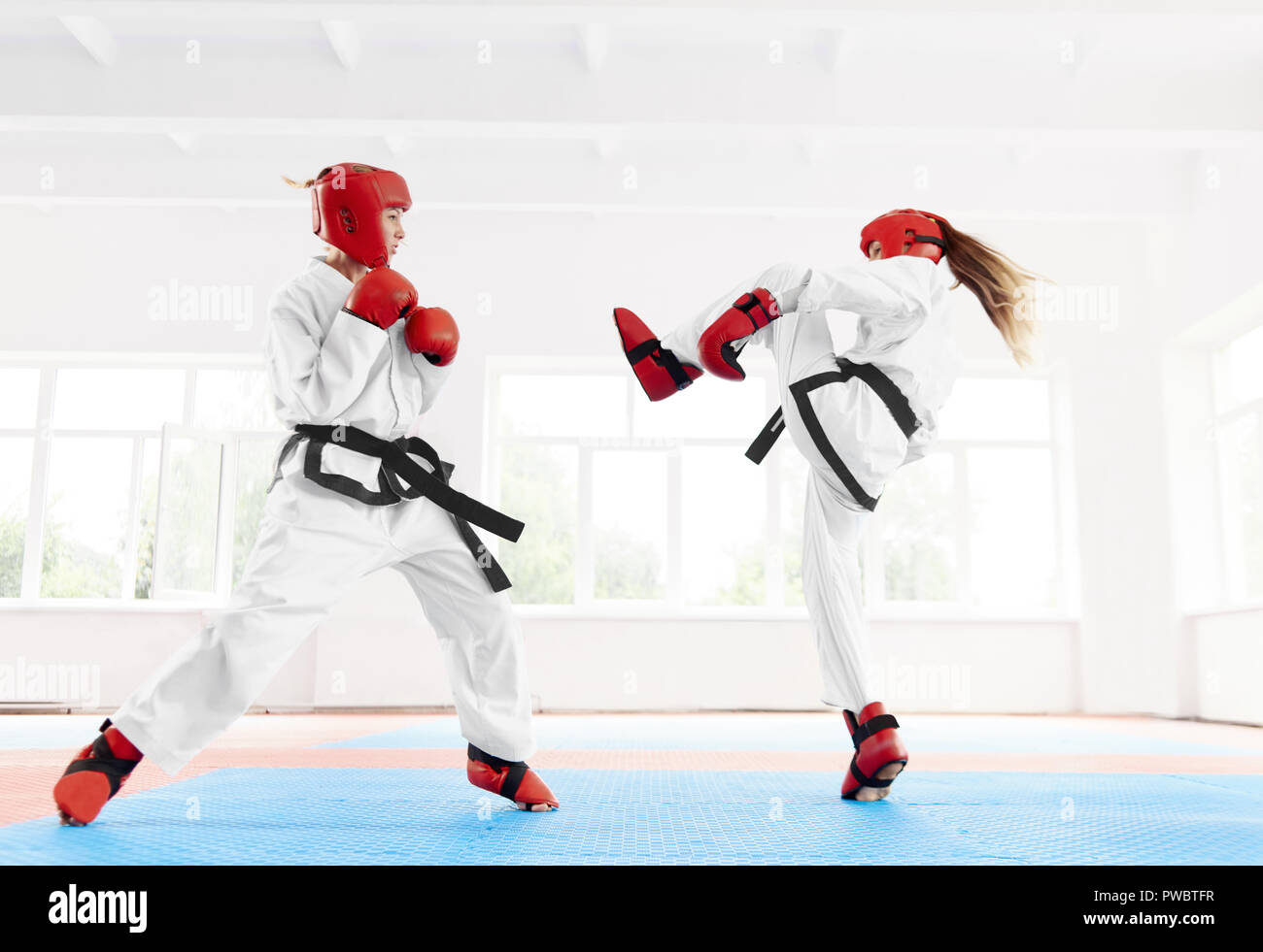 Due combattente donna indossa in kimono bianco e rosso guanti di protezione e un casco con scarpe speciali per la lotta contro la pratica del karate kick e punzone. Una ragazza in piedi mirati a colpire il suo avversario nel petto. Foto Stock