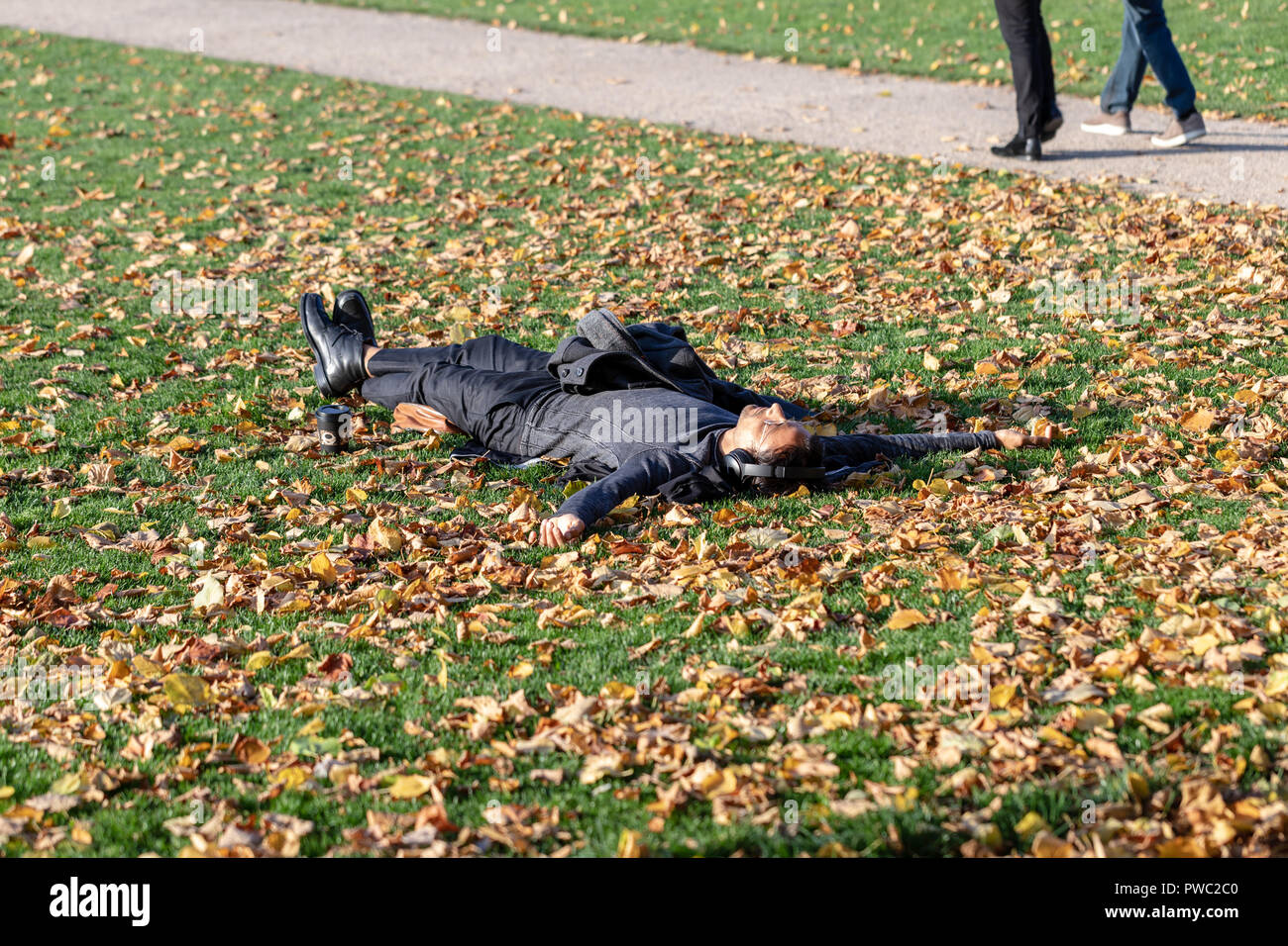 Uomo appoggiato su un parco prato cosparso con foglie Foto Stock