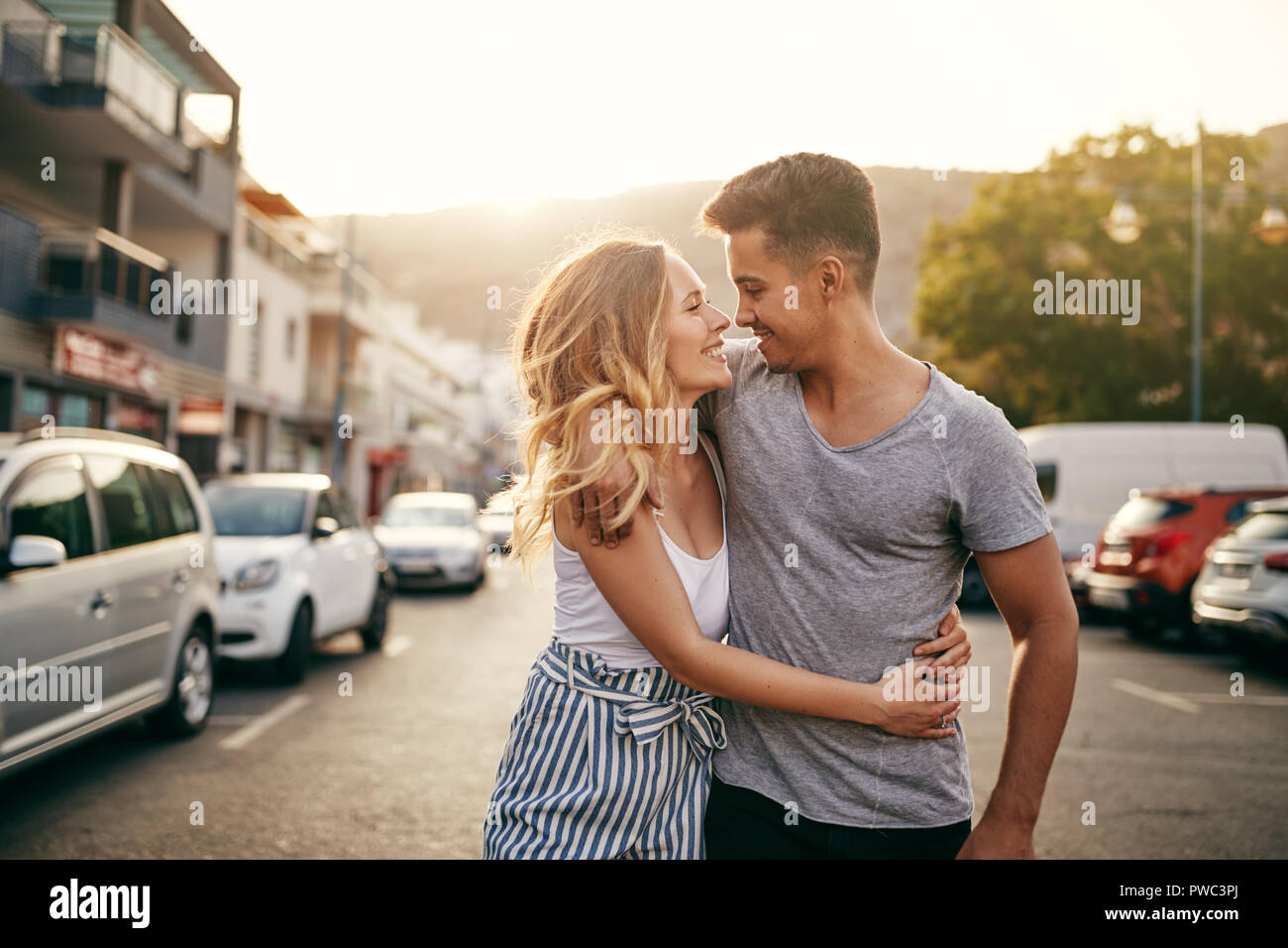 Sorridente coppia giovane camminando a braccetto insieme giù per una strada al tramonto mentre godendo una giornata insieme nella città Foto Stock