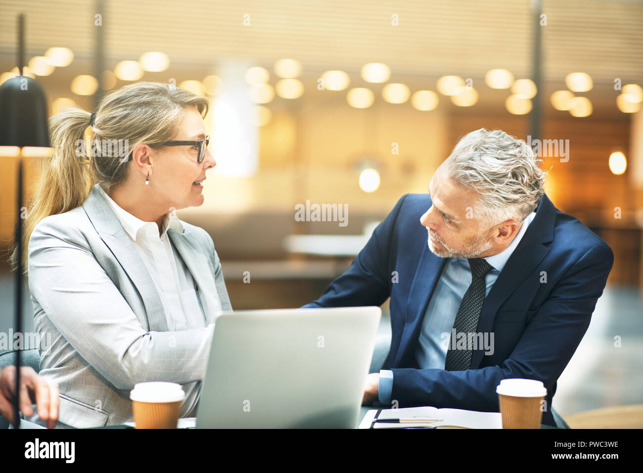 Due sorridenti imprenditori matura seduti insieme ad un tavolo in un ufficio lobby e agitando le mani insieme Foto Stock