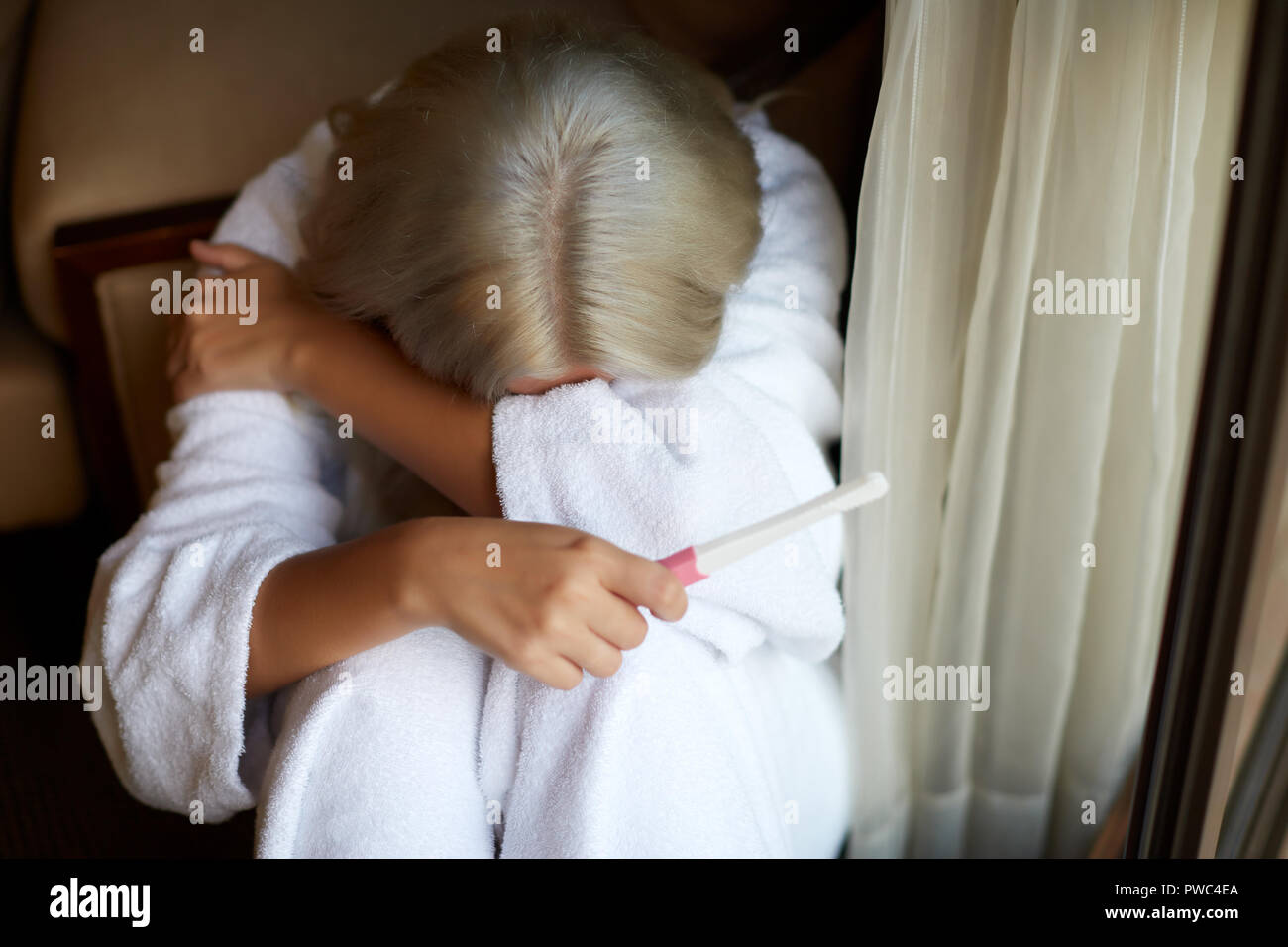 Unica donna triste lamenta tenendo un test di gravidanza di seduta su un divano nel salotto di casa Foto Stock