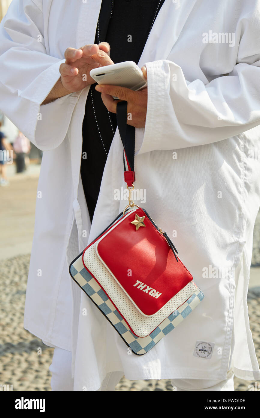 Milano, Italia - 20 settembre 2018: l'uomo con il bianco, camicia di grandi dimensioni e il rosso e il blu e bianco borsa guardando al telefono prima di Genny sfilata di moda Milano Foto Stock